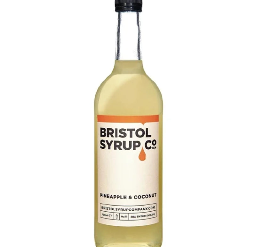 A bottle of Bristol Syrup Co. Pineapple & Coconut syrup, featuring a clear glass bottle filled with pale golden liquid, a cream-colored label with orange and black text, and a black cap, set against a plain white background.