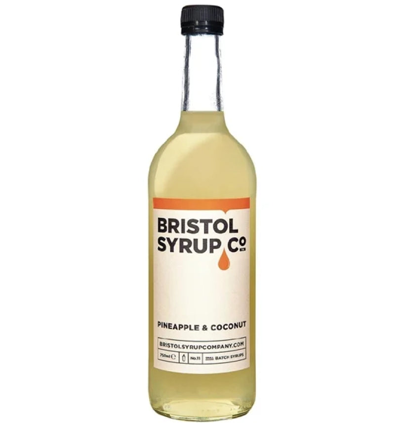 A bottle of Bristol Syrup Co. Pineapple & Coconut syrup, featuring a clear glass bottle filled with pale golden liquid, a cream-colored label with orange and black text, and a black cap, set against a plain white background.