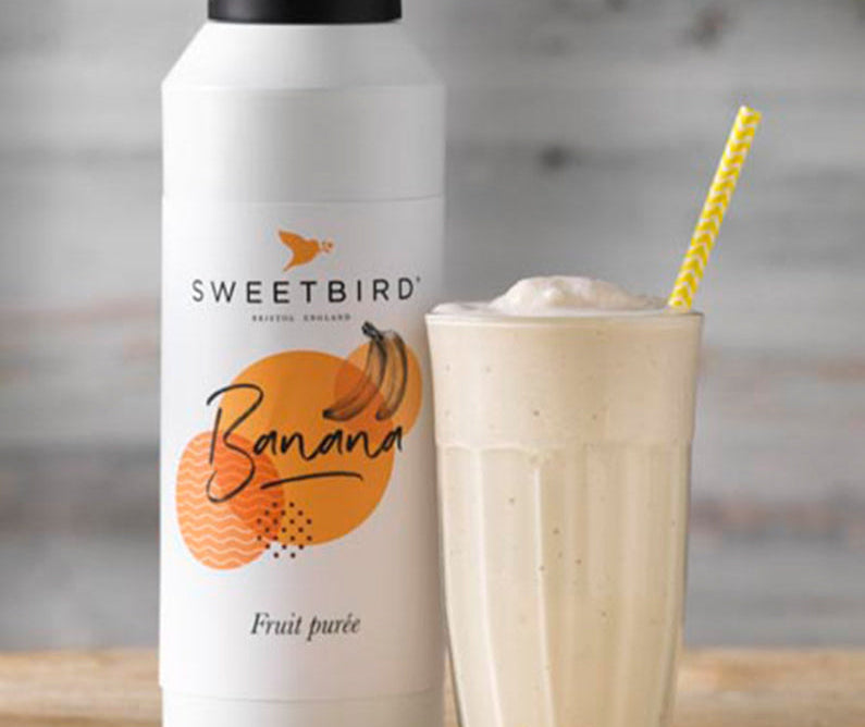 Sweetbird banana fruit juice bottle with a glass of banana smoothie on a wooden surface.
