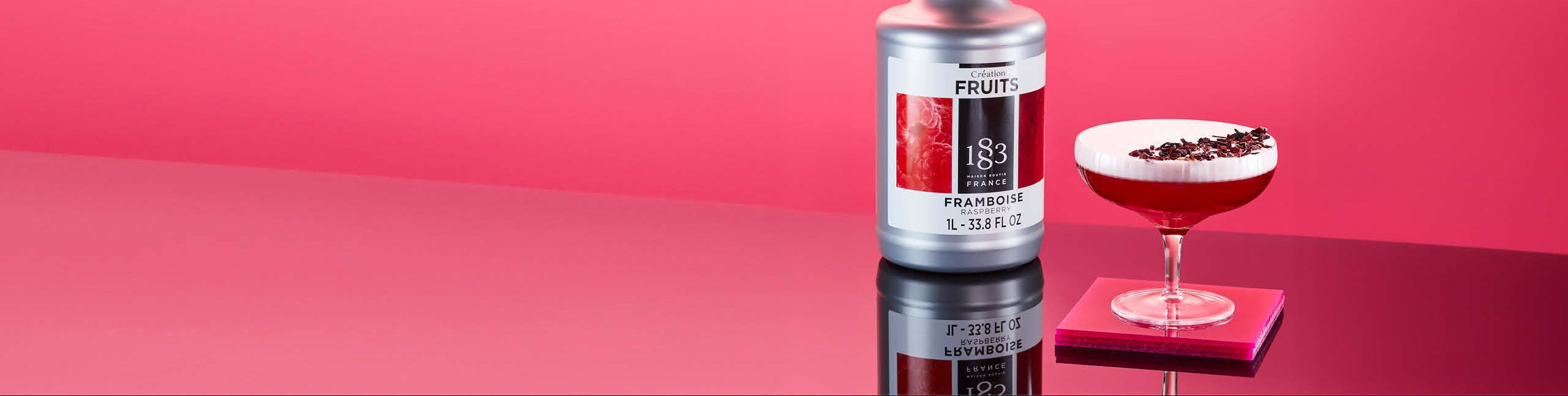Bottle of 1883 Prune Liqueur with a cocktail on a pink background